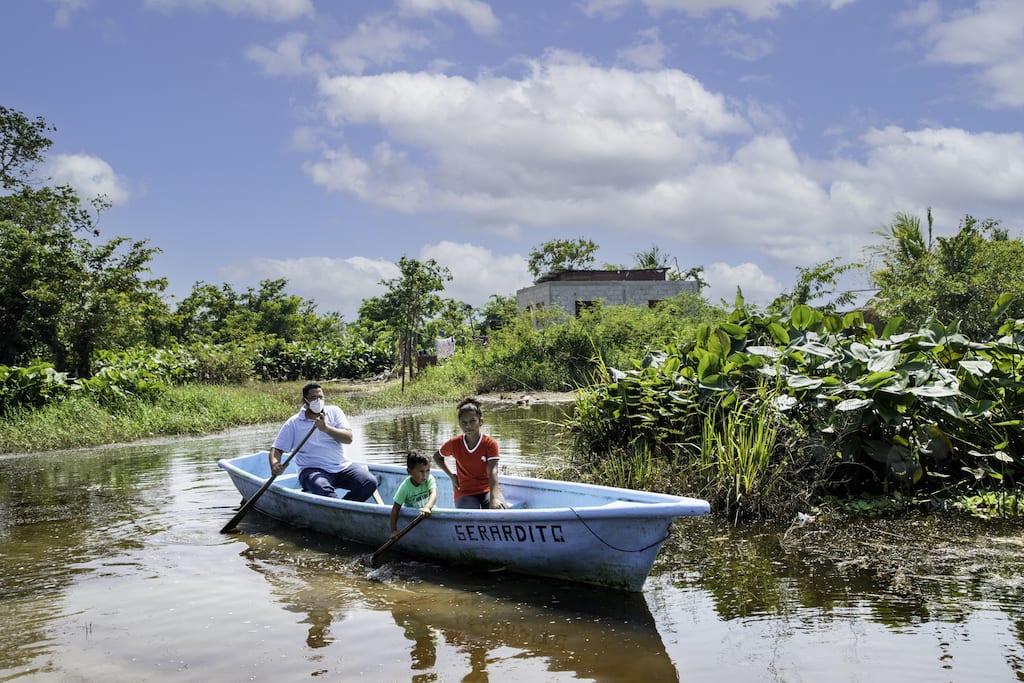 A man and two children ride a blue fishing boat through a flooded street.